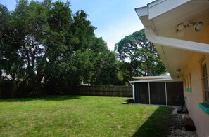 Ein Garten mit Rasenfläche, Holzzaun und einem Haus mit überdachter Terrasse.