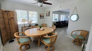 A dining area with a round table and six chairs, a ceiling fan, and a view into a living room with a sofa and a round mirror. - Flamingo House, Cozy 2/2 [pet friendly] (Sarasota)