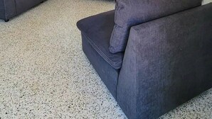Una sala de estar con un sofá modular, una mesa de centro y un televisor. Se observa un comedor al fondo con una mesa y sillas.