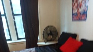 A bedroom with a bed, a window with curtains, a fan, and a poster on the wall. - Perfect 2-bedroom apartment with AC in charming Bronx neighborhood (Bronx)
