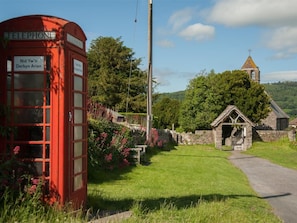 A red telephone booth with a sign, a stone building with a thatched roof, and a church tower in the background. - 2 Bed in Crickhowell (oc-bn192) (Llangynidr)