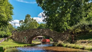 Eine steinerne Brücke über einem ruhigen Fluss, umgeben von üppigem Grün und blauem Himmel.