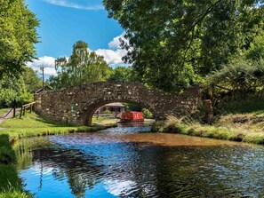 Eine steinerne Brücke über einem ruhigen Fluss, umgeben von üppigem Grün und blauem Himmel.