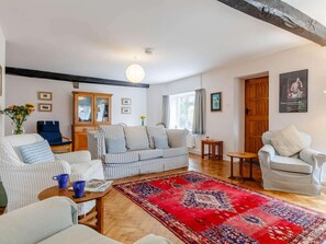 Ein Wohnzimmer mit einem gestreiften Sofa, einem roten Teppich mit Muster, einer Holzkommode und einem blauen Sessel.