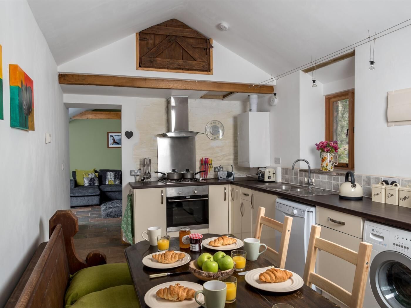 A kitchen with a dining table set for breakfast, a washing machine, and a living area with a couch.