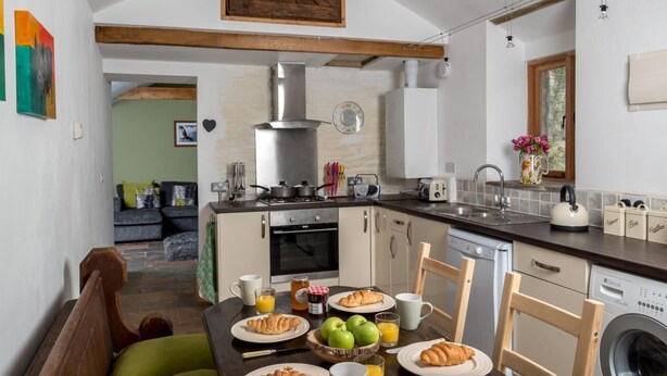 Una cocina con mesa de comedor lista para el desayuno, una lavadora y una sala de estar con sofá.