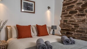 Una cama bien tendida con toallas enrolladas, un cuadro en la pared, una lámpara y un elemento decorativo de pared de piedra.