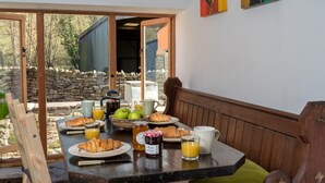 Una mesa de desayuno con cruasanes, jugo y mermelada, ubicada en una habitación con muebles de madera y pared de piedra.