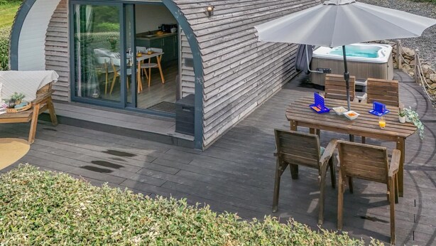 A cozy, semi-open structure with a glass door leading to a dining area, a hot tub, and a wooden deck.