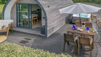 A cozy, semi-open structure with a glass door leading to a dining area, a hot tub, and a wooden deck.