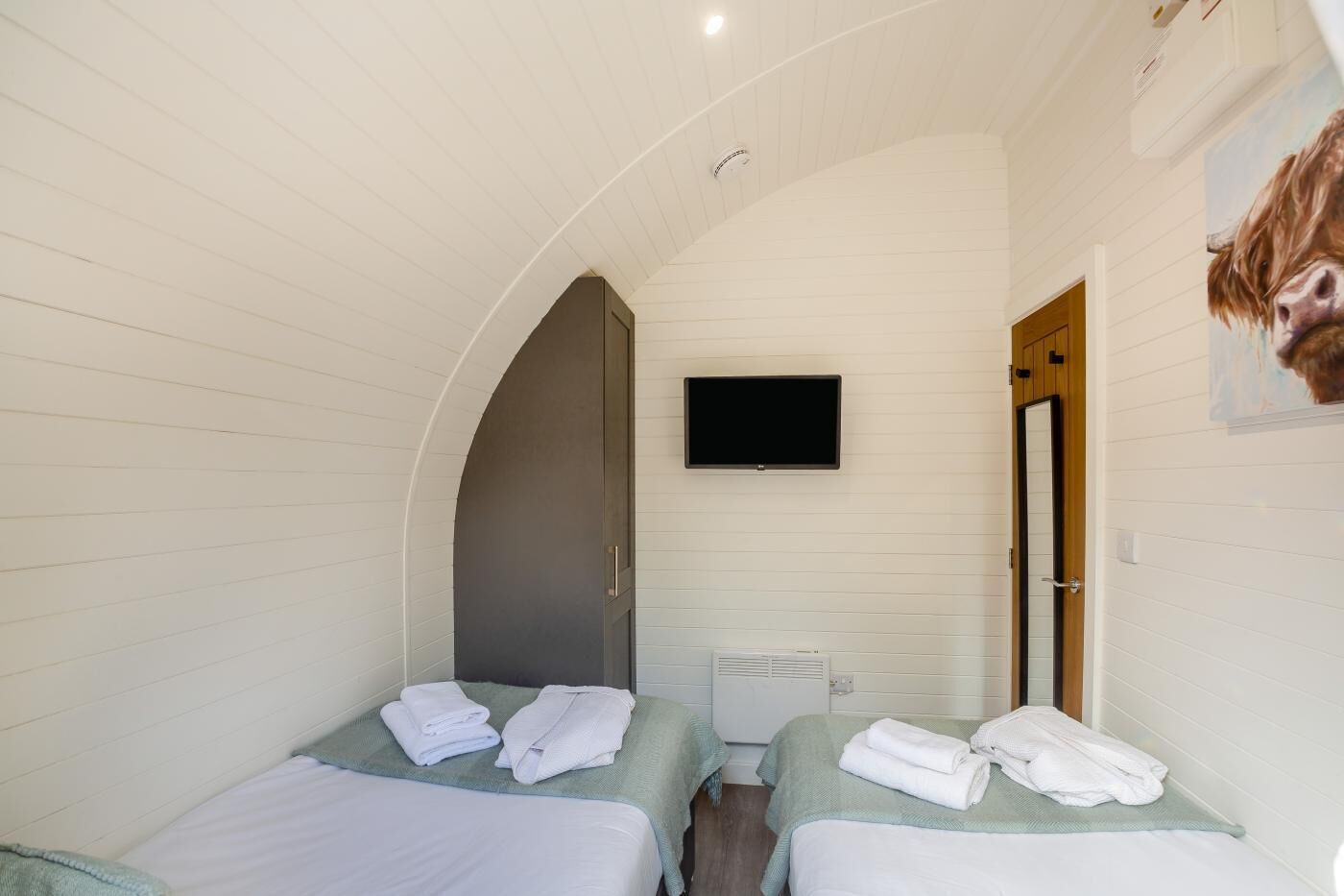A room with two beds, a TV, an arched doorway, and a cow painting.