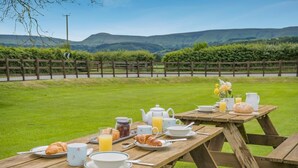 A picnic setup with a table, plates, cups, and food items. - 3 Bed in Brecon (oc-bn370) (Llyswen)