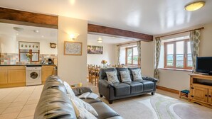 A living room with a sofa, a television, and a kitchen area with a washing machine. - 3 Bed in Brecon (oc-bn370) (Llyswen)