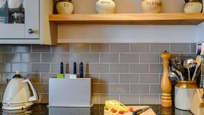 Eine Küche mit Kaffeemaschine, Toaster, Schneidebrett mit Gemüse und Gläsern auf einem Regal.