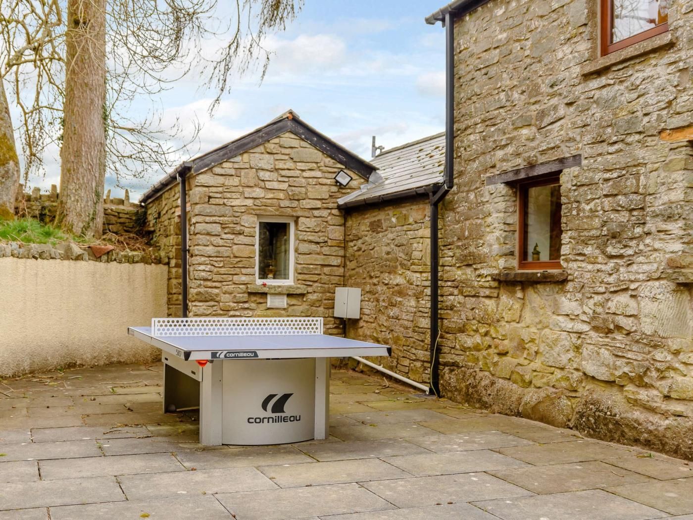 Une table de ping-pong installée dans un espace extérieur, avec des bâtiments en pierre en arrière-plan.