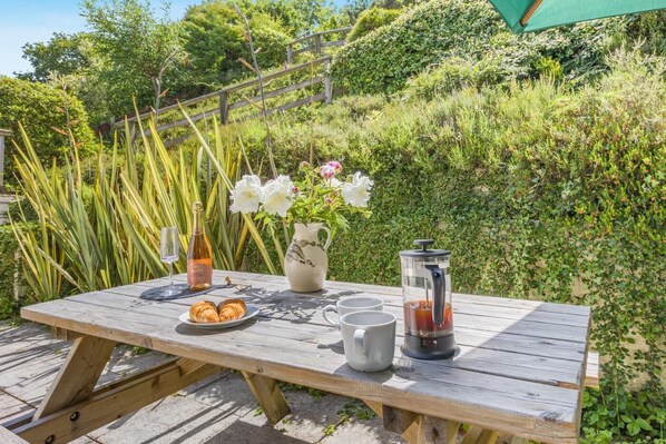 A wooden picnic table with a bottle, a pitcher, a teapot, and a plate of pastries.