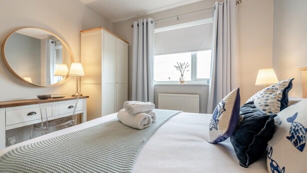 Une chambre d’hôtel avec un lit, une coiffeuse avec un miroir, une fenêtre avec des rideaux et un radiateur.