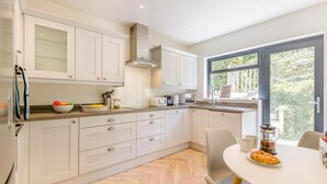Une cuisine moderne avec des meubles blancs, un parquet en chevrons et un coin repas comprenant une table et des chaises.