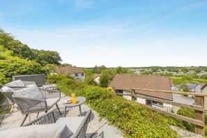 Eine Dachterrasse mit Korbmöbeln, einem Tisch mit einem Getränk und Blick auf Häuser und Grünflächen.