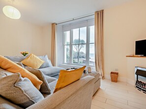 A living room with a sofa, a television, a window with curtains, and a view of the outdoors. - 1 Bed in Tenby (oc-fb021) (Tenby)