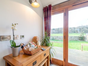 Ein Zimmer mit einem Holztisch, einem Korb voller Gegenstände, einer Topf-Orchidee und Blick auf eine grüne Landschaft durch eine Glastür.