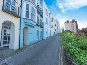 A narrow cobblestone street lined with colorful buildings, a clear sky, and a stone wall on one side. - 2 Bed in Tenby (oc-fb114) (Tenby)