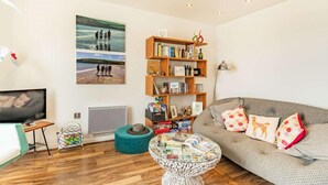 A living room with a sofa, a coffee table, a bookshelf, a TV, and a painting on the wall. - 2 Bed in Tenby (oc-fb110) (Tenby)