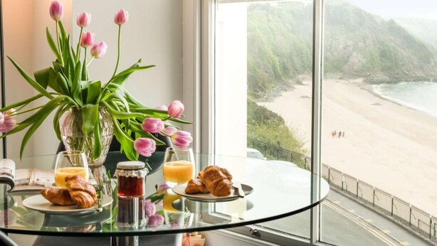 A breakfast table with croissants, juice, and jam, overlooking a beach. - 2 Bed in Tenby (oc-fb110) (Tenby)