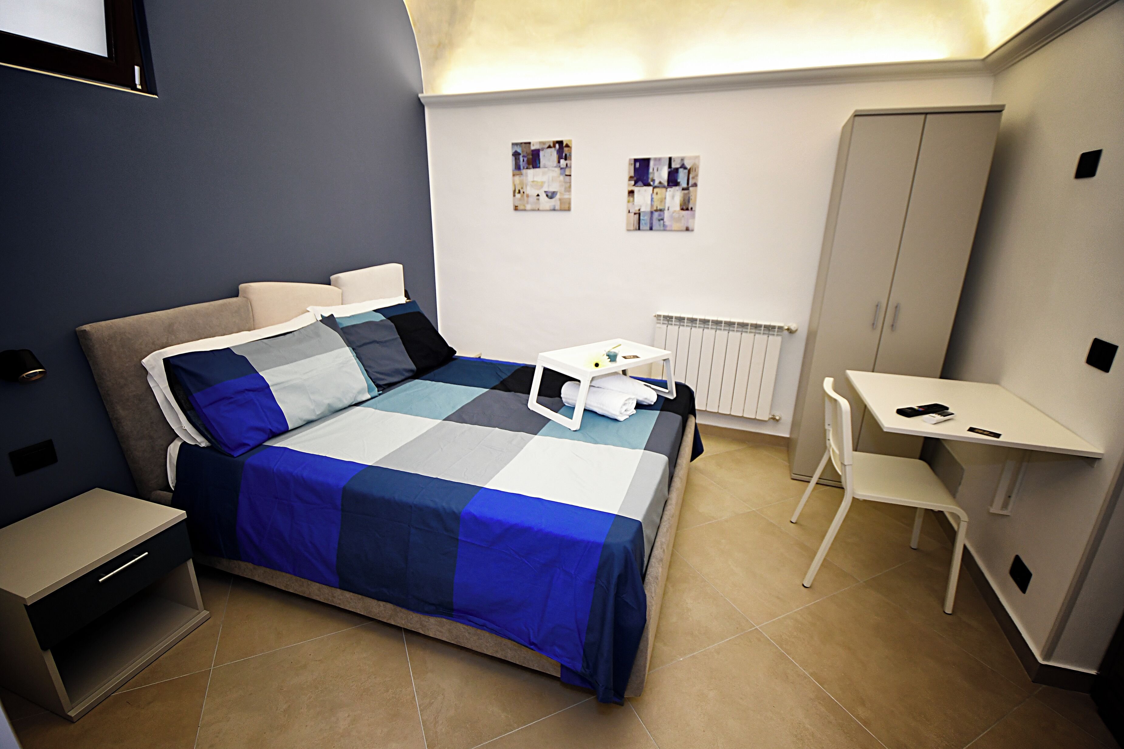 Un dormitorio con cama, mesita de noche, silla, escritorio y armario.