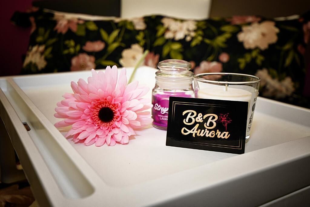 Een dienblad met een roze bloem, een kaars met de tekst 'B&B Aurora' en een klein flesje lavendelolie.