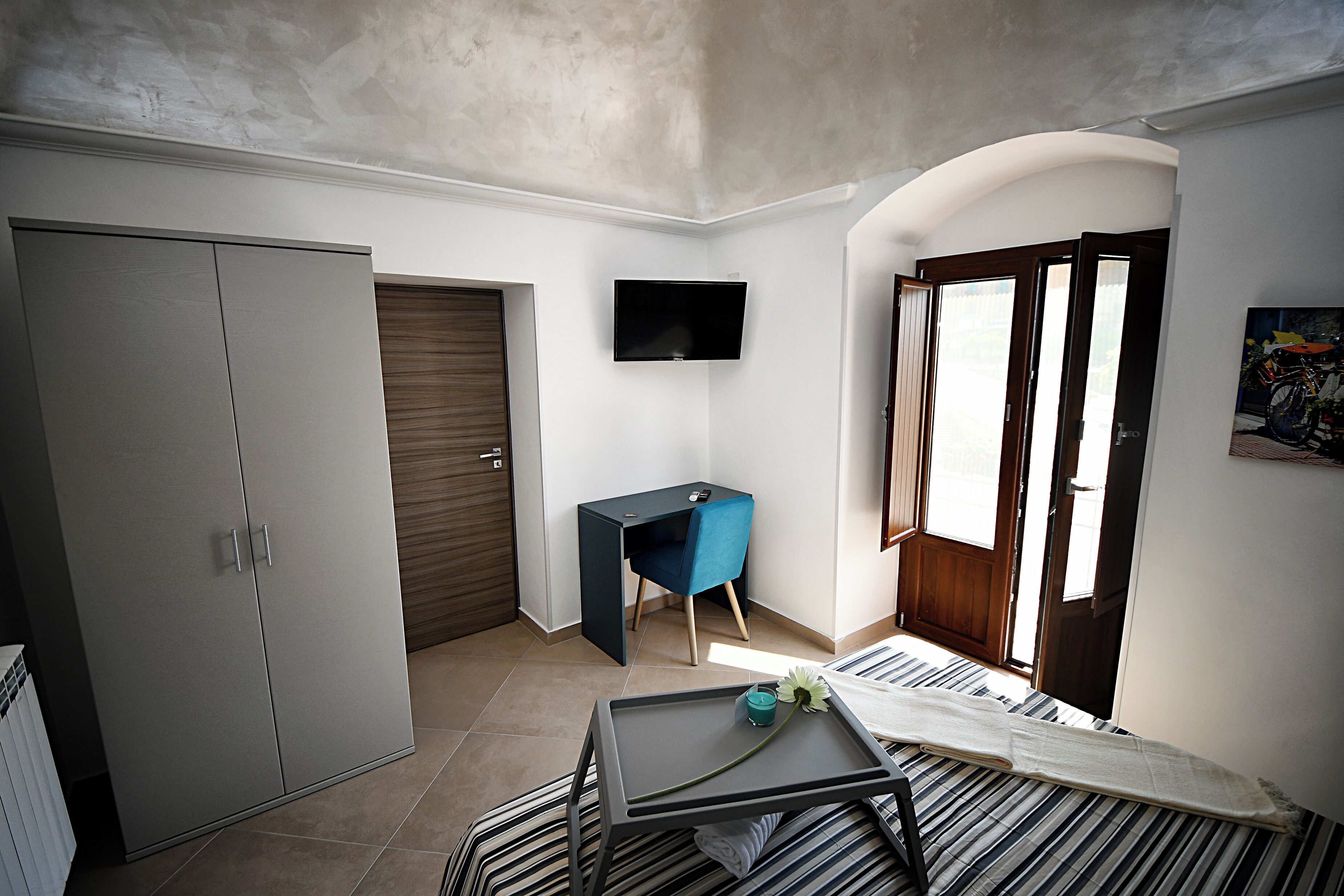 A bedroom with a bed, a desk, a wardrobe, a TV, and a window with a view.