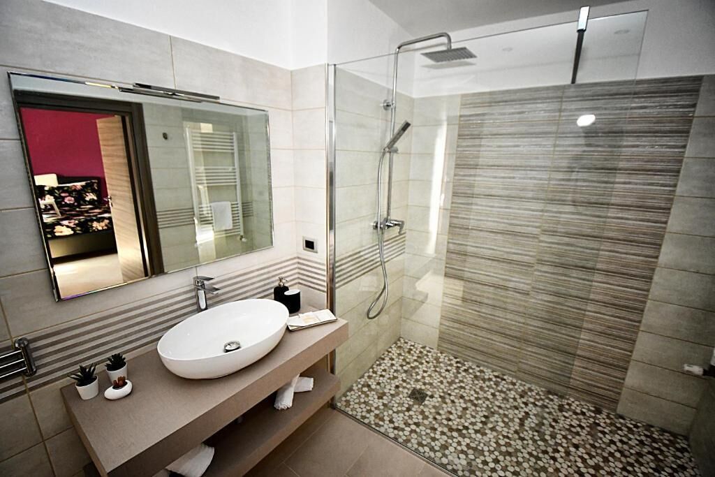 A modern bathroom with a glass-enclosed shower, a large mirror, and a beige vanity.