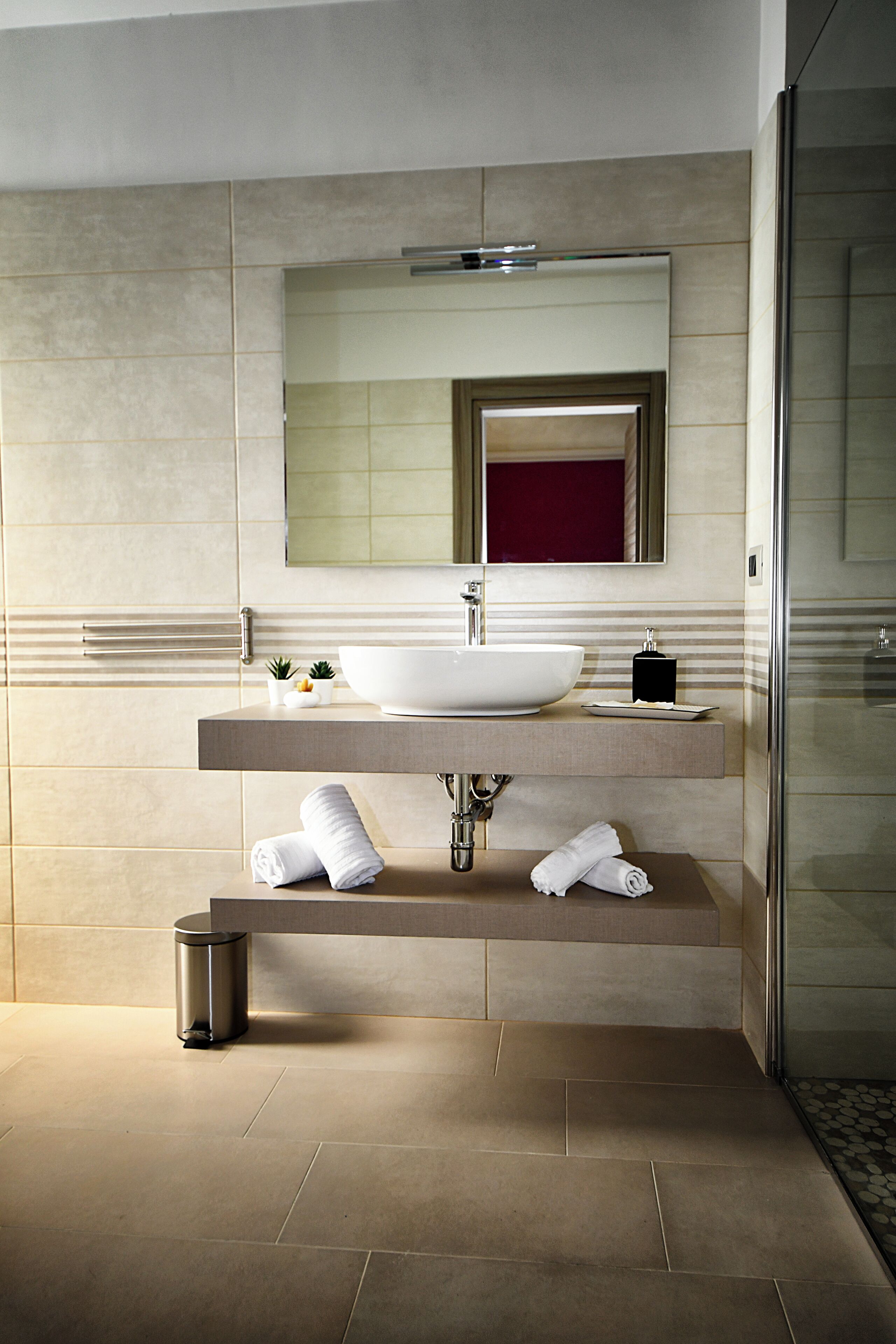 A modern bathroom with a large white sink, a mirror above it, and a glass shower door.