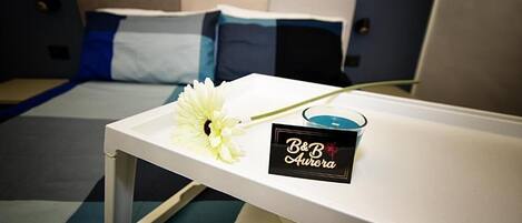 A hotel room with a bed, a bedside table with a flower and a candle, and a sign reading 'B&B Aurora'.
