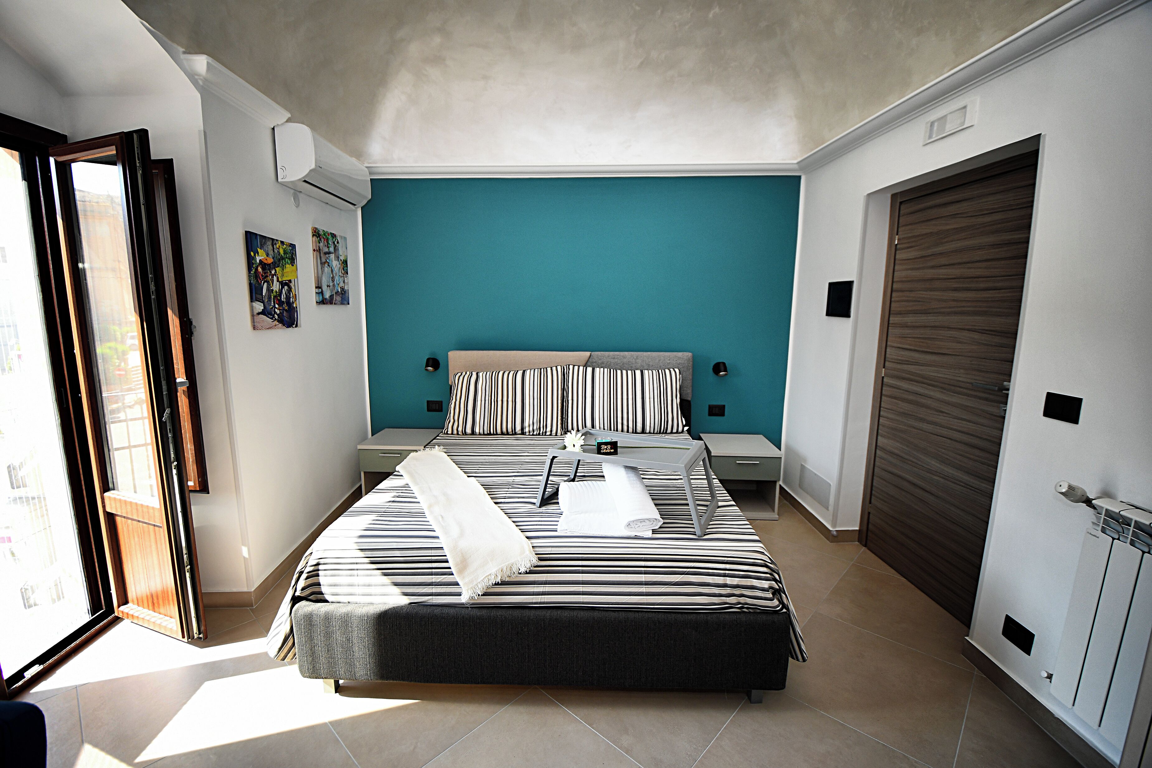A bedroom with a bed, a bedside table, a nightstand, a window, and a door.