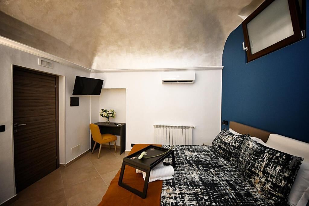 Quarto compacto com cama, escrivaninha, cadeira, televisão e radiador.