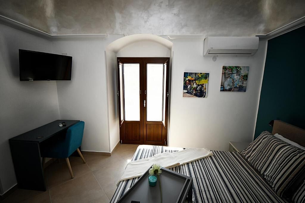 A bedroom with a bed, a desk, a TV, and a door leading to a balcony.