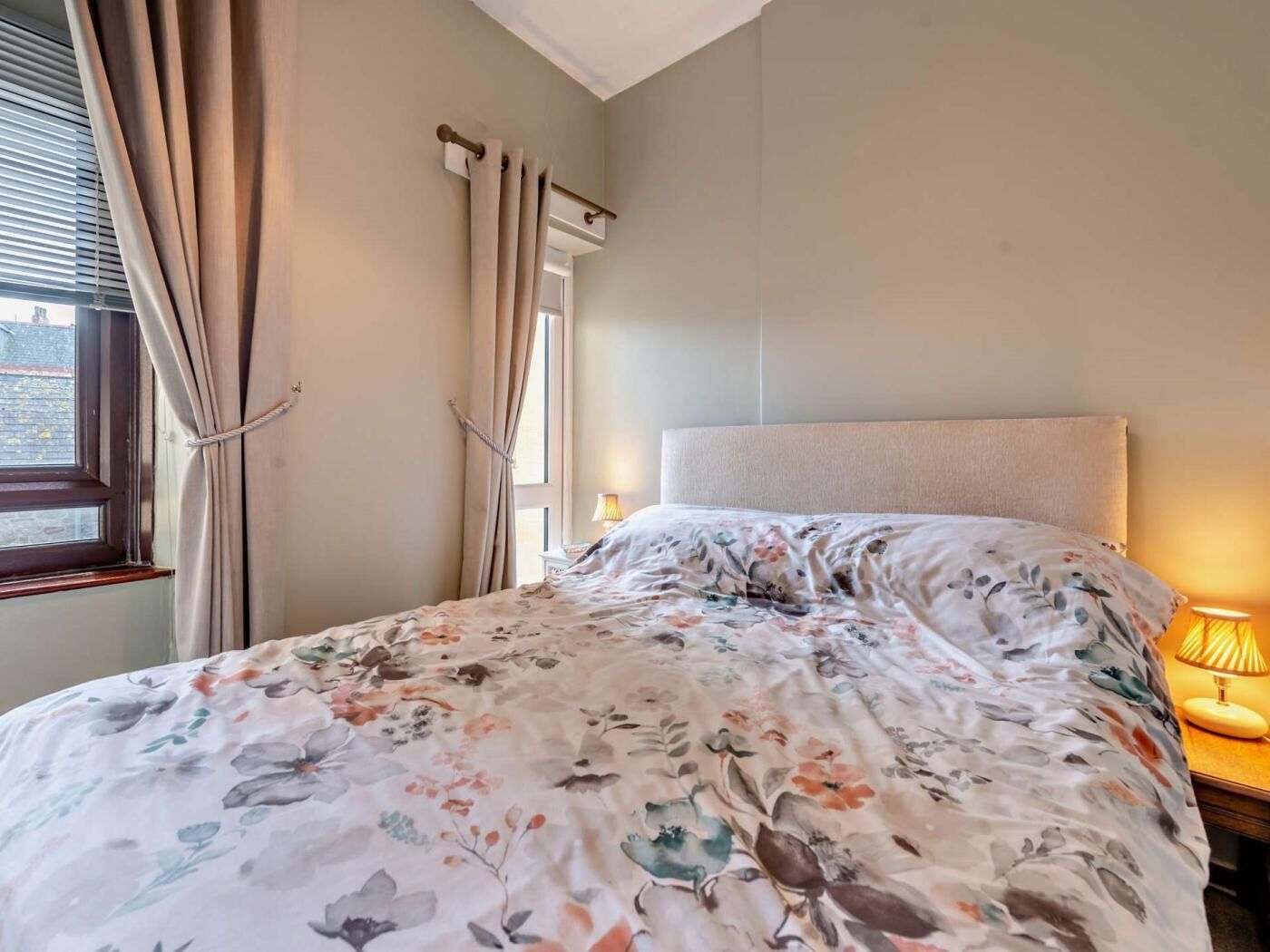 A bedroom with a bed, curtains, a window, and a bedside lamp.