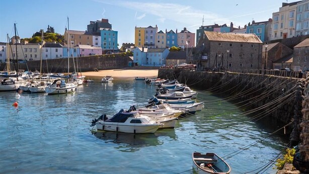 A harbor with boats docked, colorful buildings, and a sandy beach in the background. - 2 Bed in Tenby (oc-fb122) (Tenby)