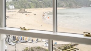 A coastal view through a window with a sandy beach, boats, and buildings in the background. - 2 Bed in Tenby (oc-fb113) (Tenby)