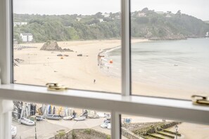 Blick durch ein Fenster auf die Küste mit einem Sandstrand, Booten und Gebäuden im Hintergrund.