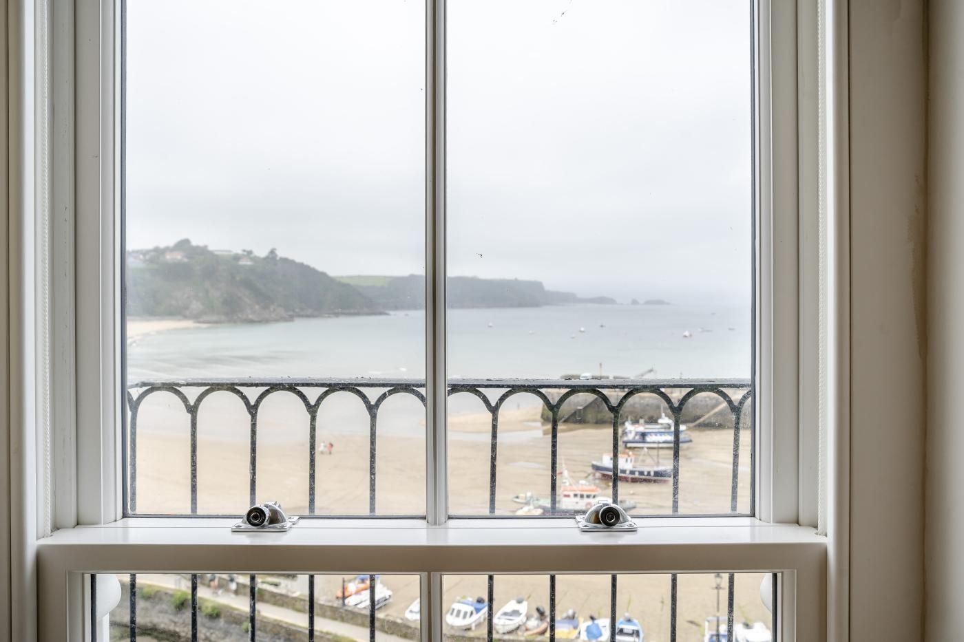 Une fenêtre donnant sur une plage et des bateaux, avec une balustrade au premier plan.