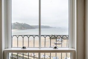 Ein Fenster mit Blick auf einen Strand und Boote, mit einem Geländer im Vordergrund.