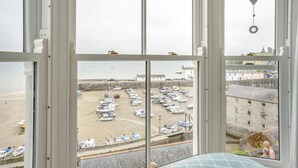 A view from a window overlooking a marina with boats docked, a sandy beach, and a stone building in the background. - 2 Bed in Tenby (oc-fb113) (Tenby)