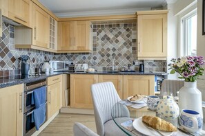 Eine moderne Küche mit Holzausstattung, einer gefliesten Spritzschutzwand und einem Essbereich mit Tisch und Stühlen, gedeckt für das Frühstück.
