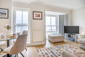 Ein modernes Wohnzimmer mit einem Glastisch, einer bequemen Couch, einem Fernseher und Meerblick.
