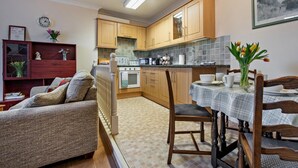 Un espacio habitable compacto con kitchenette, comedor y zona de estar con sofá y sillas.