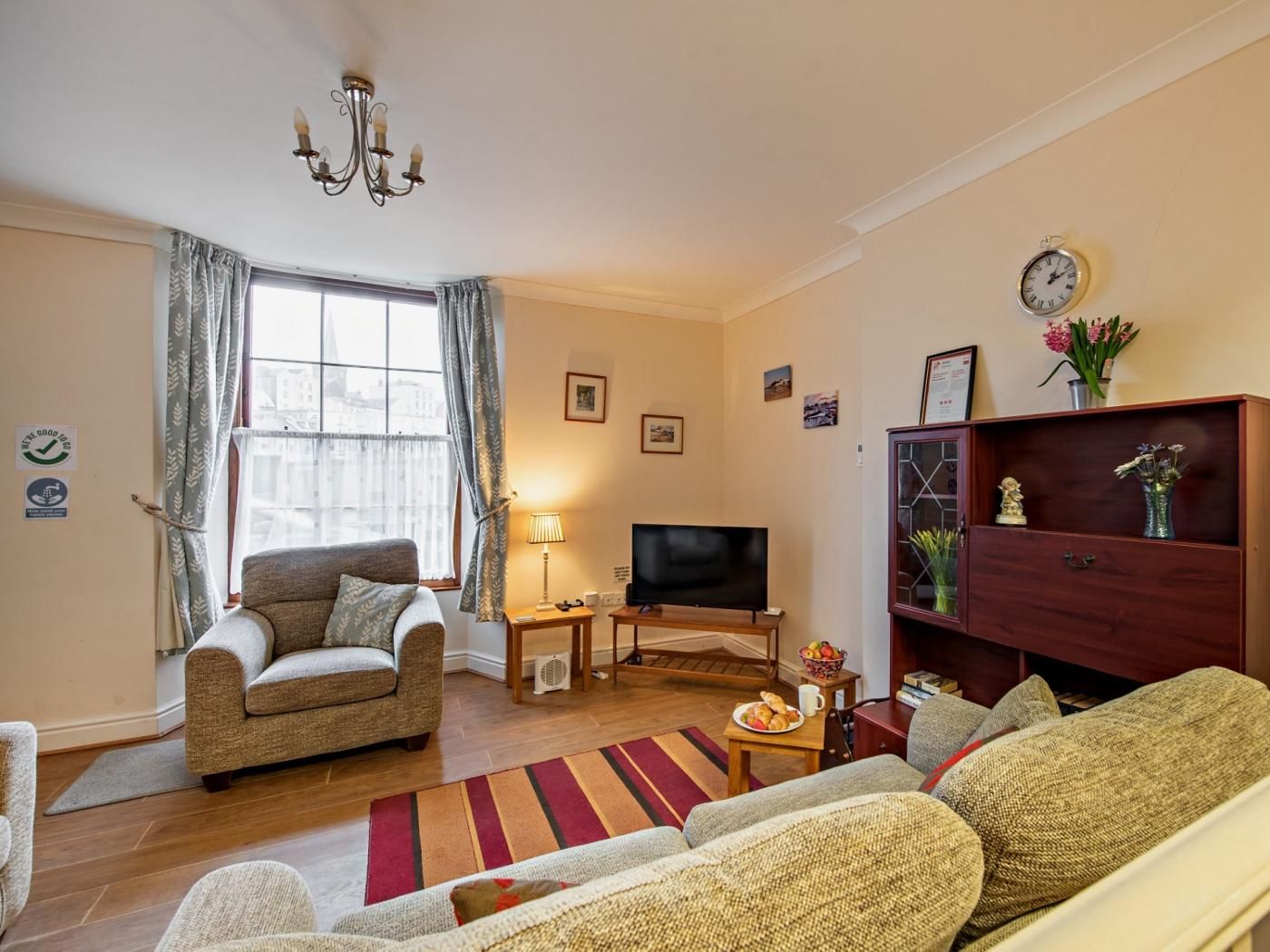 A living room with a sofa, a television, a wooden cabinet, and a window with curtains.