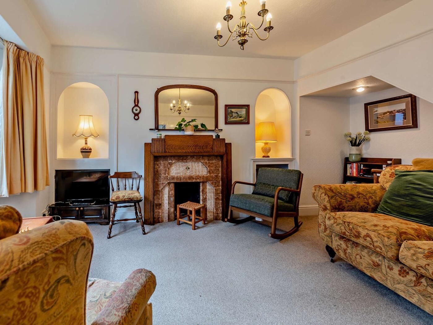 A living room with a fireplace, two armchairs, a sofa, a television, and a chandelier.