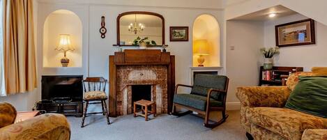 A living room with a fireplace, two armchairs, a sofa, a television, and a chandelier.